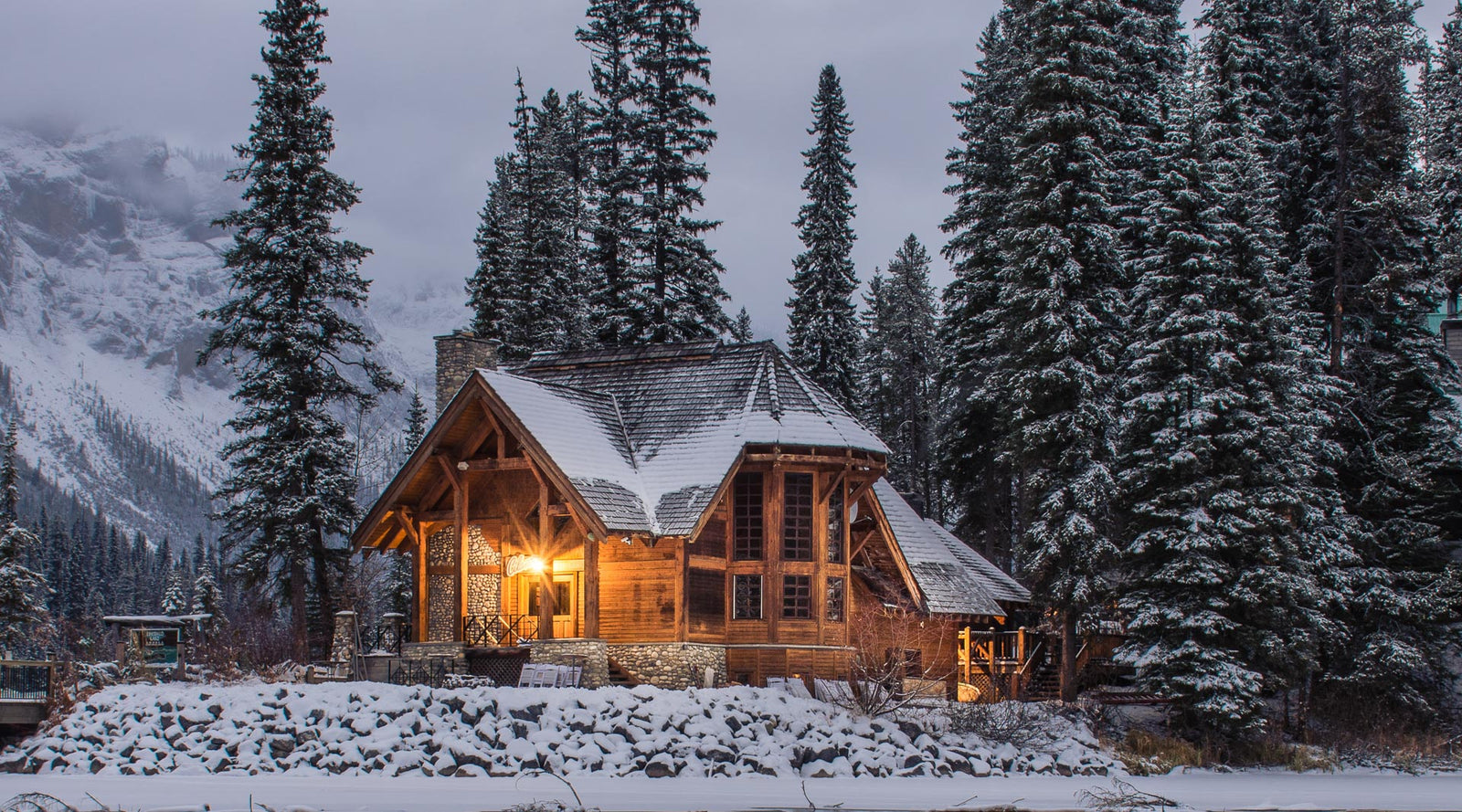 Wooden House Surrounded by Trees and Snowy Mountains in Winter